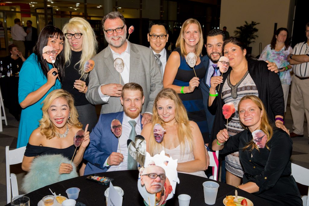 Group of people at event holding cutout face props and smiling around table.