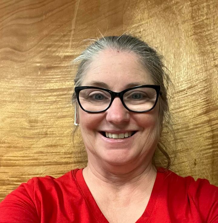 Woman with gray hair and black-rimmed glasses smiling in red t-shirt selfie portrait.