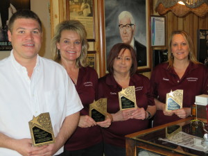 Restaurant team of four staff members in burgundy uniforms holding awards and books.