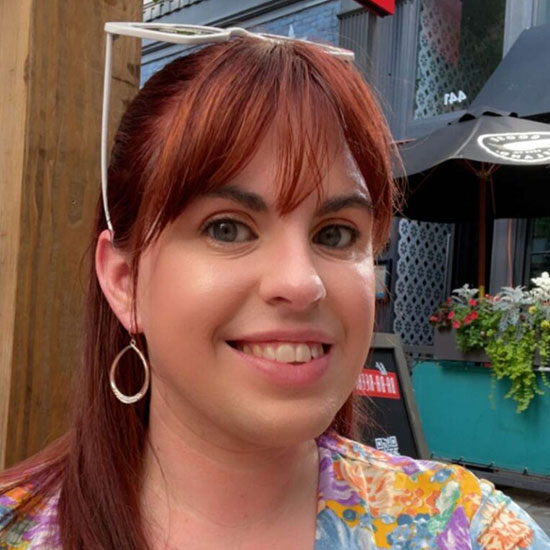 Woman smiling outdoors wearing colorful floral top and hoop earrings.