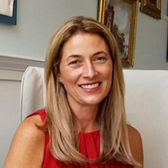 Woman with long straight blonde hair in red sleeveless top smiling in home setting.