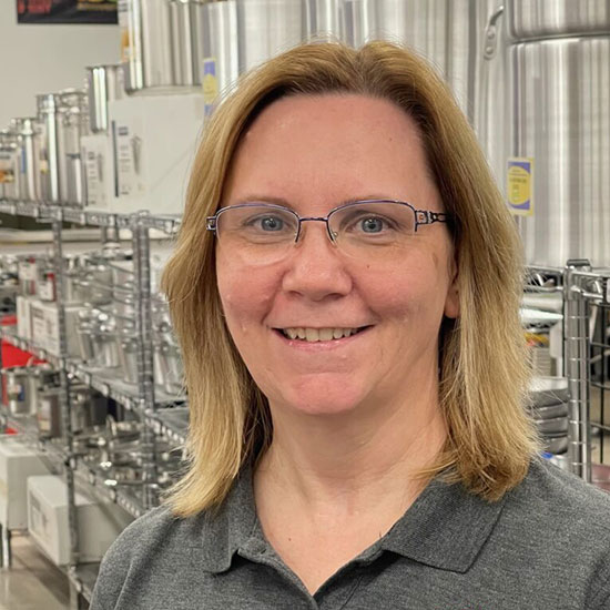 Woman with glasses smiling in industrial bottling facility with stainless steel equipment.