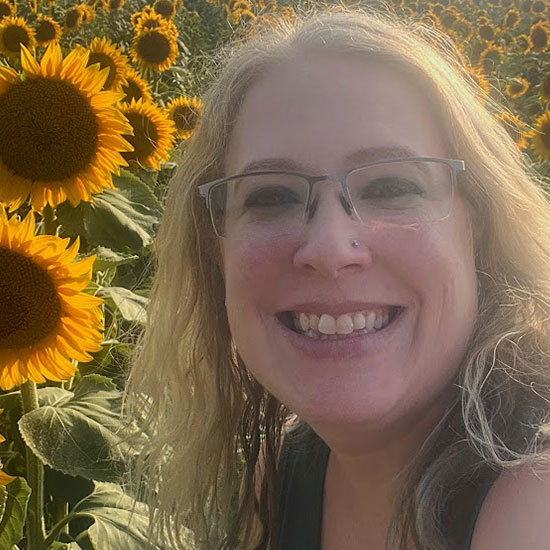Close-up of smiling woman with glasses in a sunflower field on a sunny day.