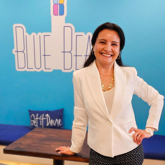 Professional woman in a white blazer standing in front of a bright blue wall with the words ‘Blue Bean.