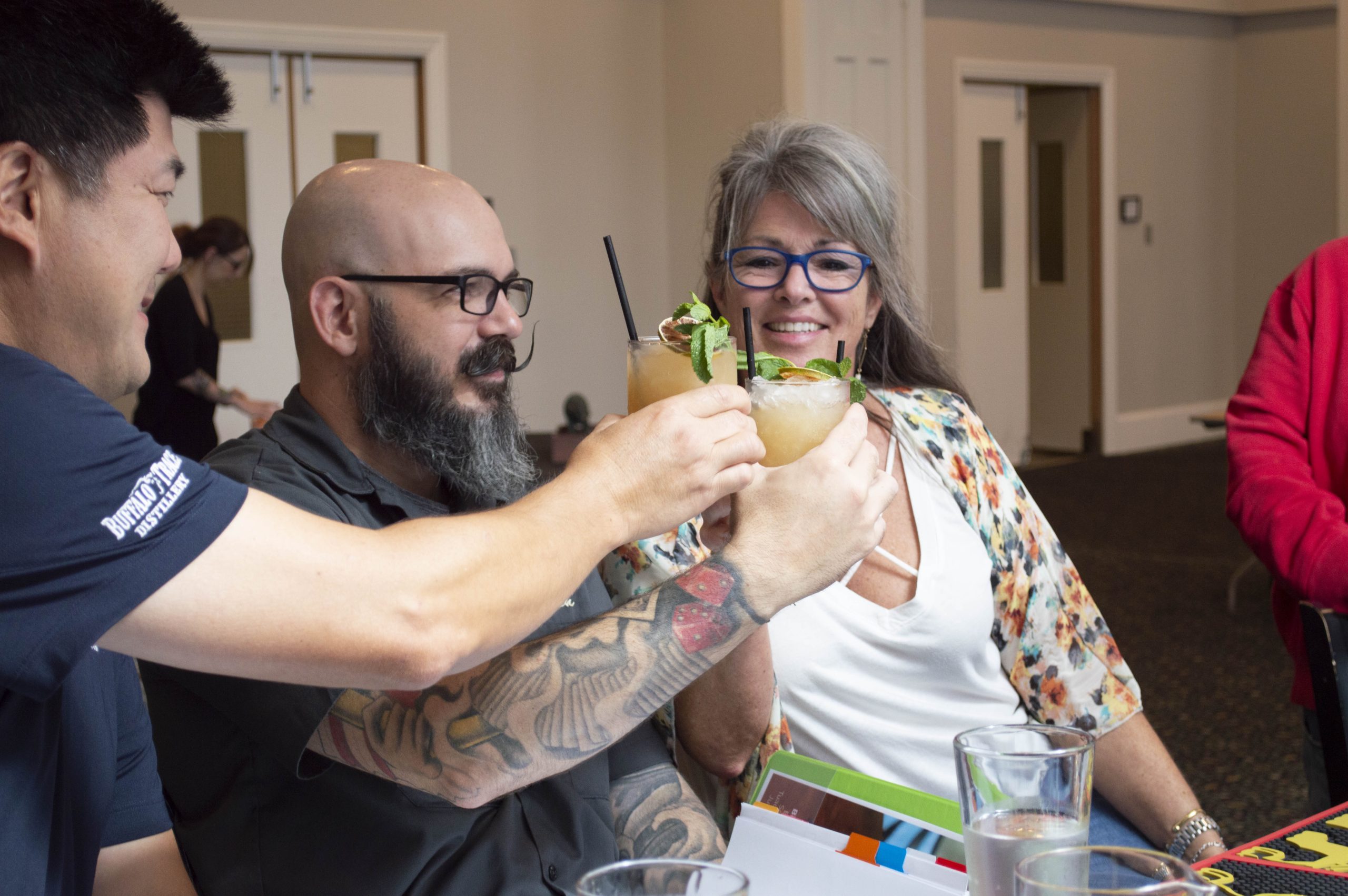 Friends smiling and raising glasses of cocktails garnished with mint and lime in a celebratory toast.