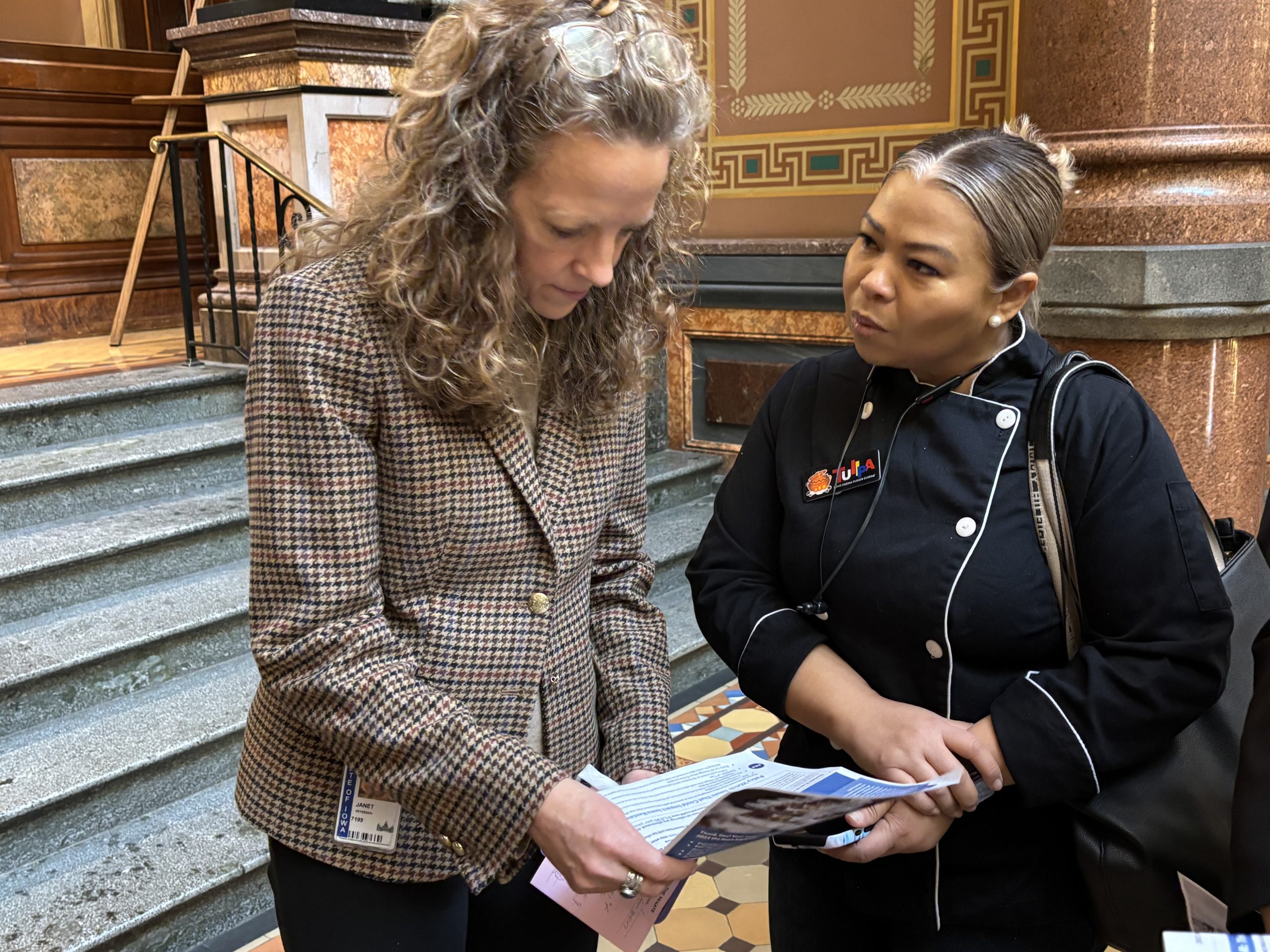 Two women standing in a historic building, reviewing printed documents together.