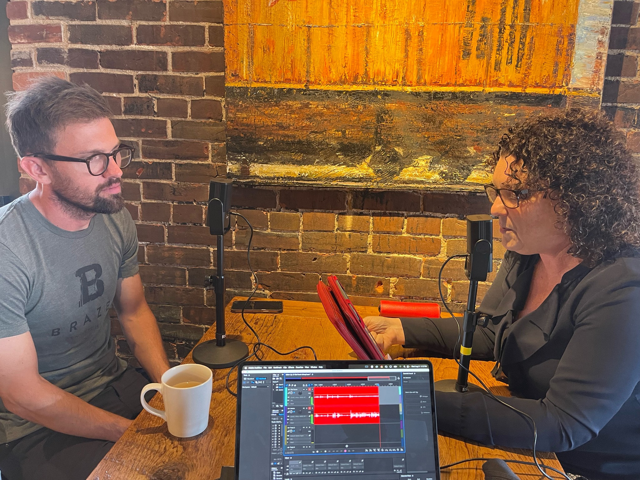 Two people recording a podcast at a table with microphones and laptop setup.