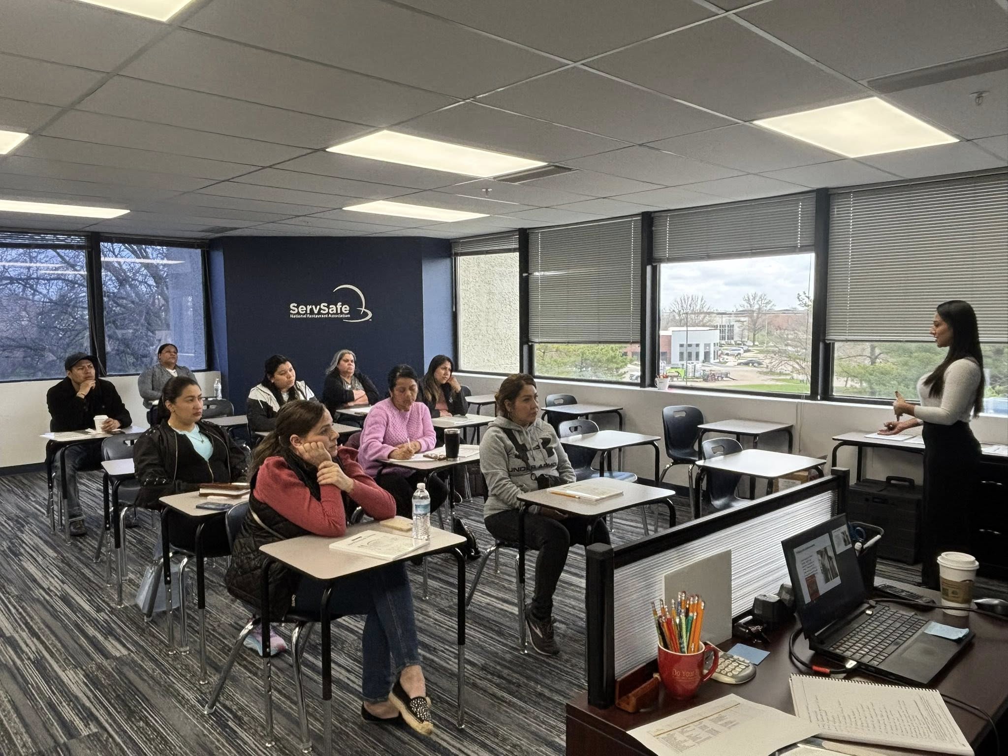 Classroom of adults attending a ServSafe food safety training session with instructor at front.