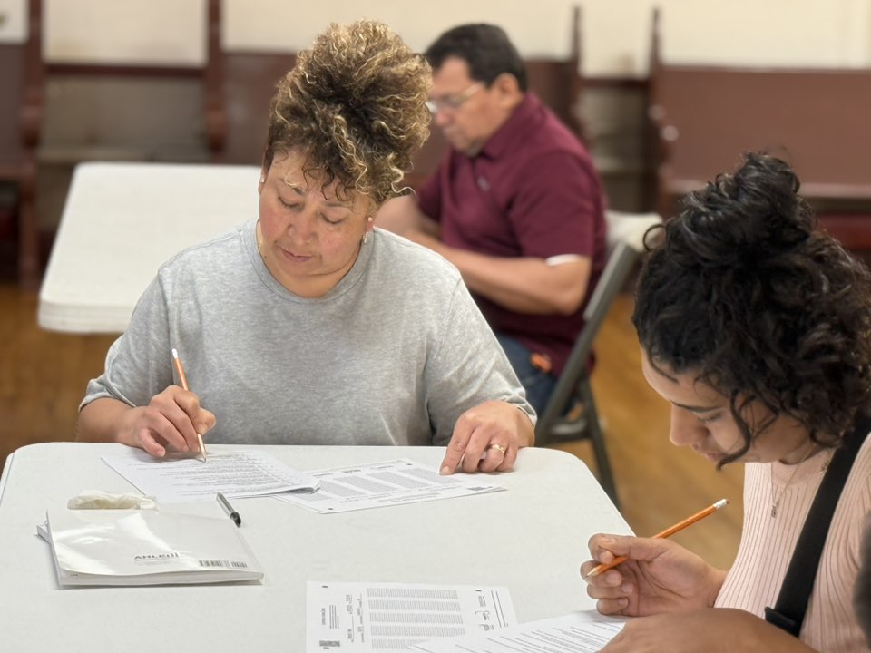 Adults seated at tables filling out paperwork during Spanish-language ServSafe class.