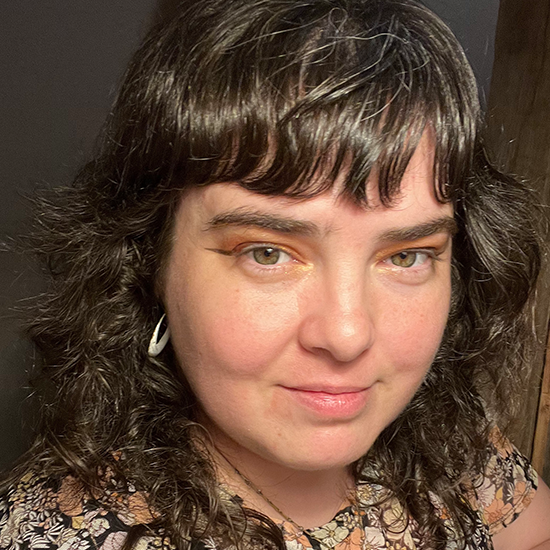 Close-up portrait of a woman with curly dark hair and bangs, wearing patterned clothing and hoop earrings.