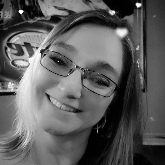 Black and white photo of a smiling woman with glasses and straight hair, wearing hoop earrings.