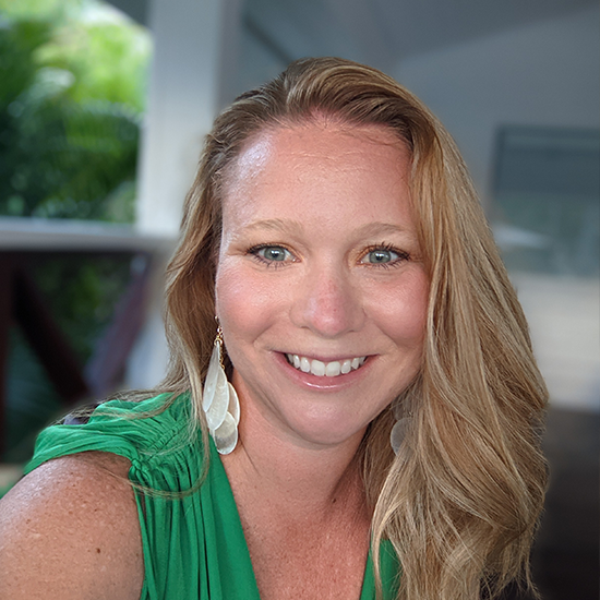 Woman smiling in a green sleeveless top with long blonde hair, photographed outdoors near a covered patio.